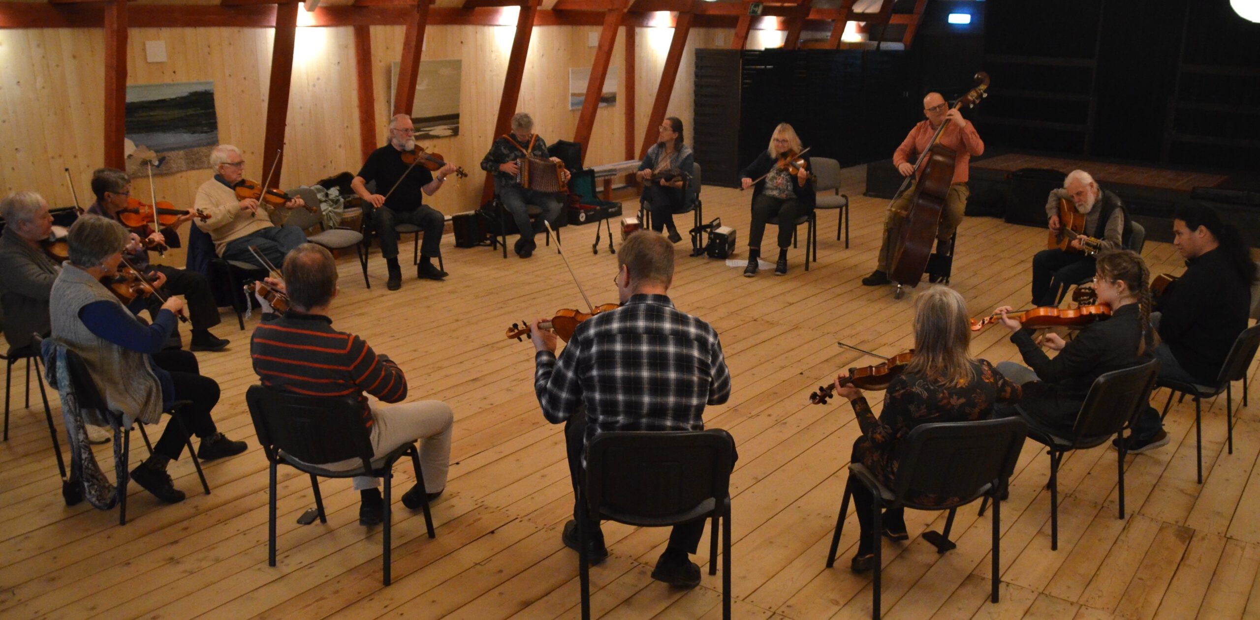 Cirka femton spelmän sitter i ring och spelar fiol, durspel, kontrabas och gitarr.