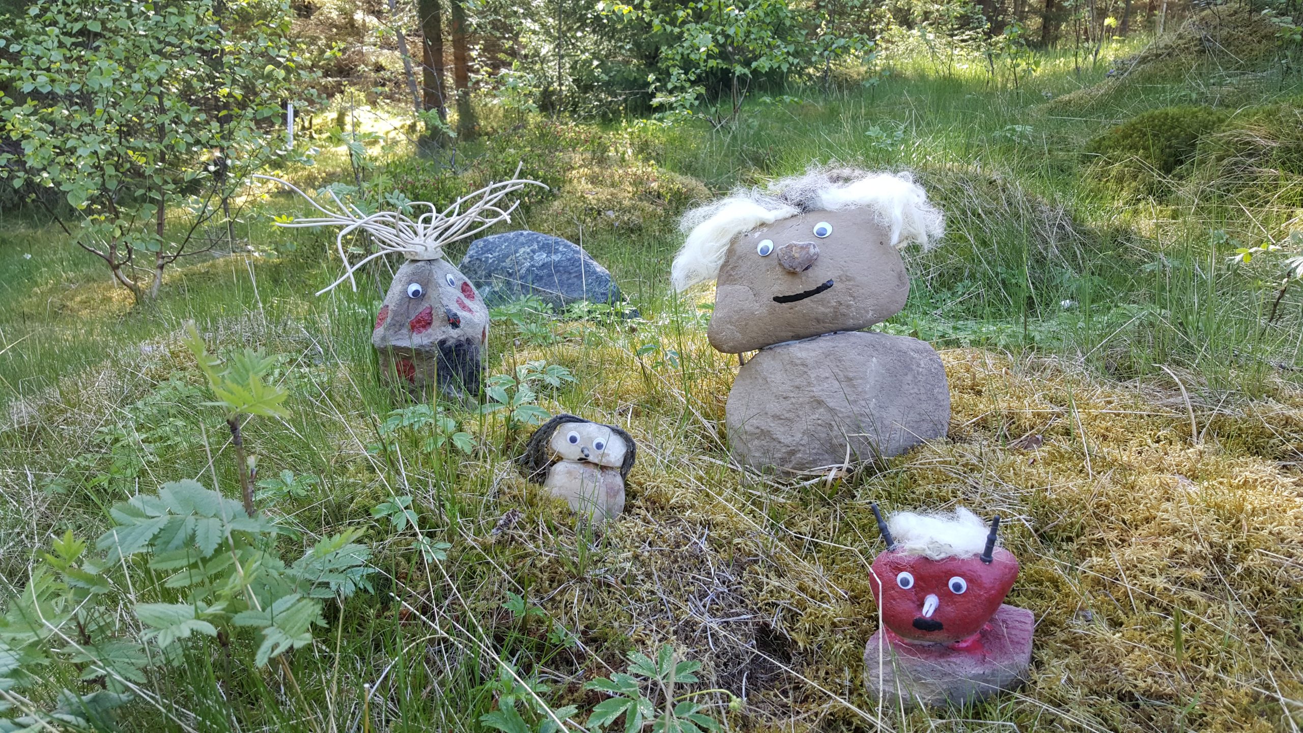 Fyra olika troll gjorda av sten sitter i gräset.